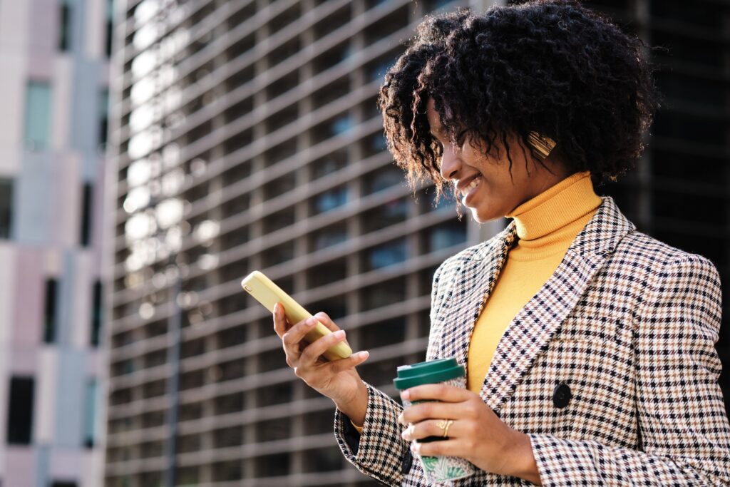 A businesswoman in a blazer looks at her phone while holding a cup of coffee.