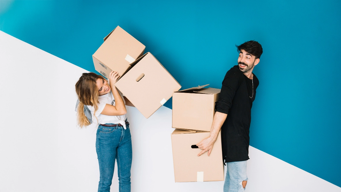 Two people playfully carrying moving boxes.